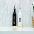 Black and white opaque glass oil and vinegar dispenser bottles on a smooth bamboo tray