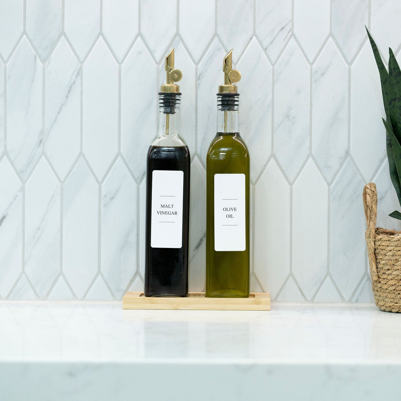 Two 500ml clear glass oil and vinegar bottles with metal pourers on a natural bamboo tray