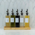 5-piece clear glass oil and vinegar bottle set with precision pourers on a natural bamboo tray