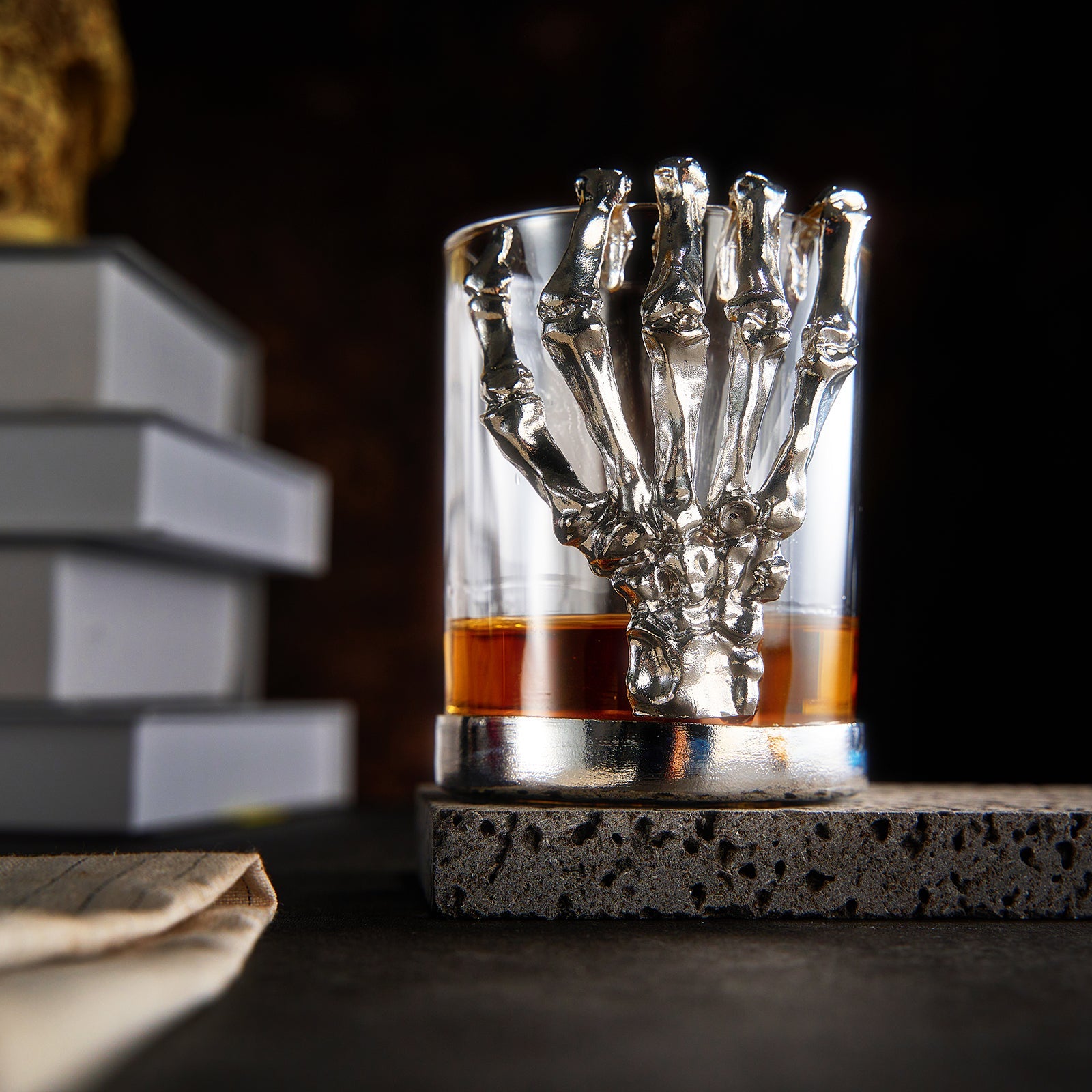 Skeleton whiskey glass tumbler with detailed bone hand stem, clear glass cup holding amber liquor — view 2