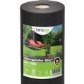 Water-permeable weed barrier fleece unrolled on a garden bed for landscaping and weed prevention.