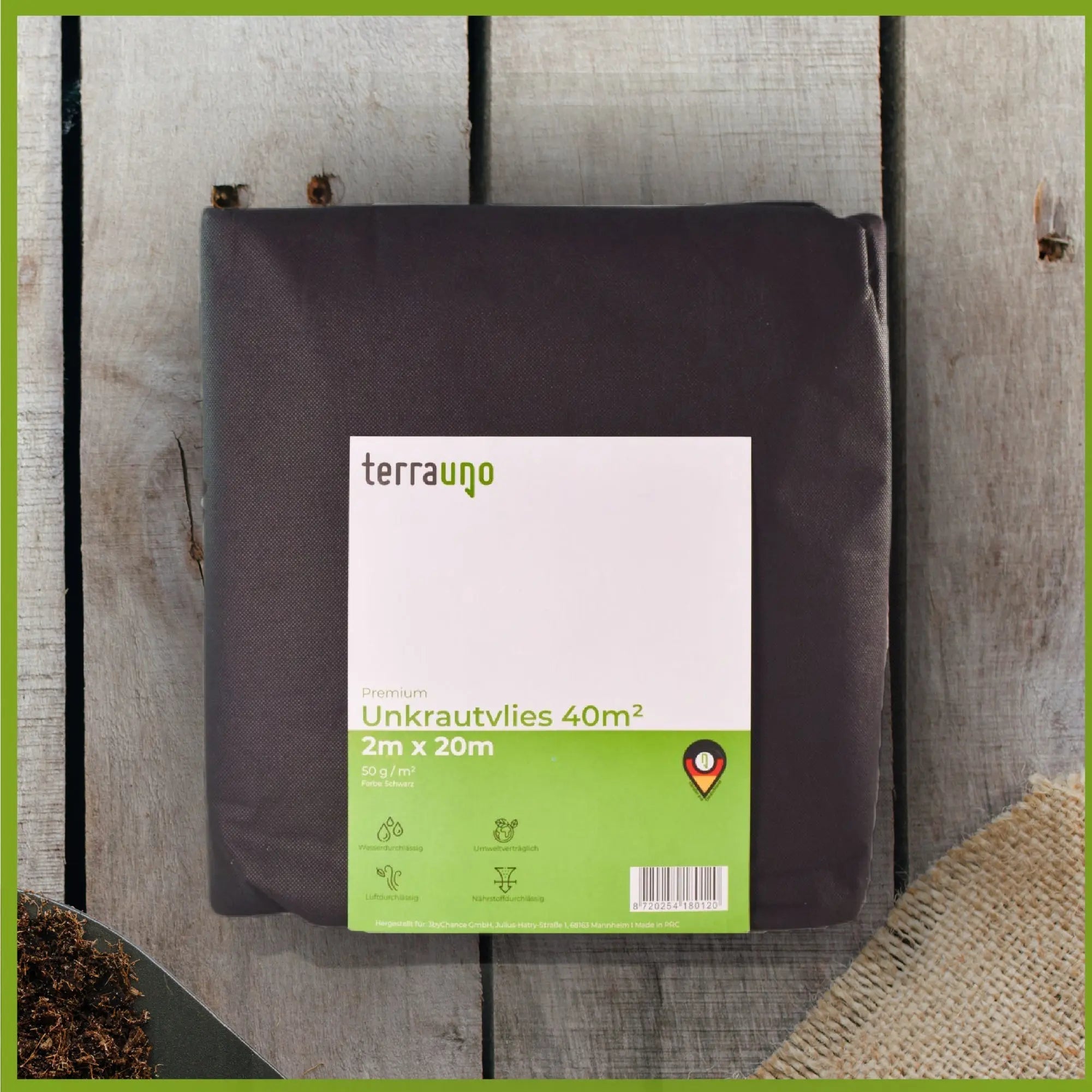 Water-permeable weed barrier fleece unrolled on a garden bed for landscaping and weed prevention. — view 3