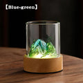 Blue-green glass mountain ambient night light with a solid wood base and glowing warm illumination