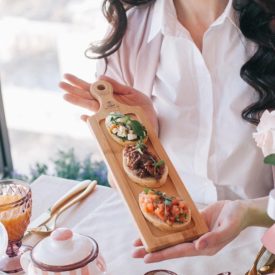 Rectangular natural bamboo serving tray with handle for appetizers and sliders on a table