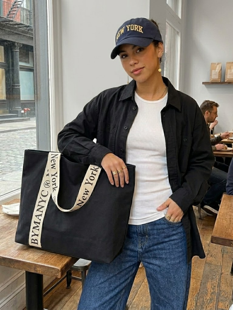 Women's black canvas tote bag with wide cream straps and bold typographic logo lettering. — view 2