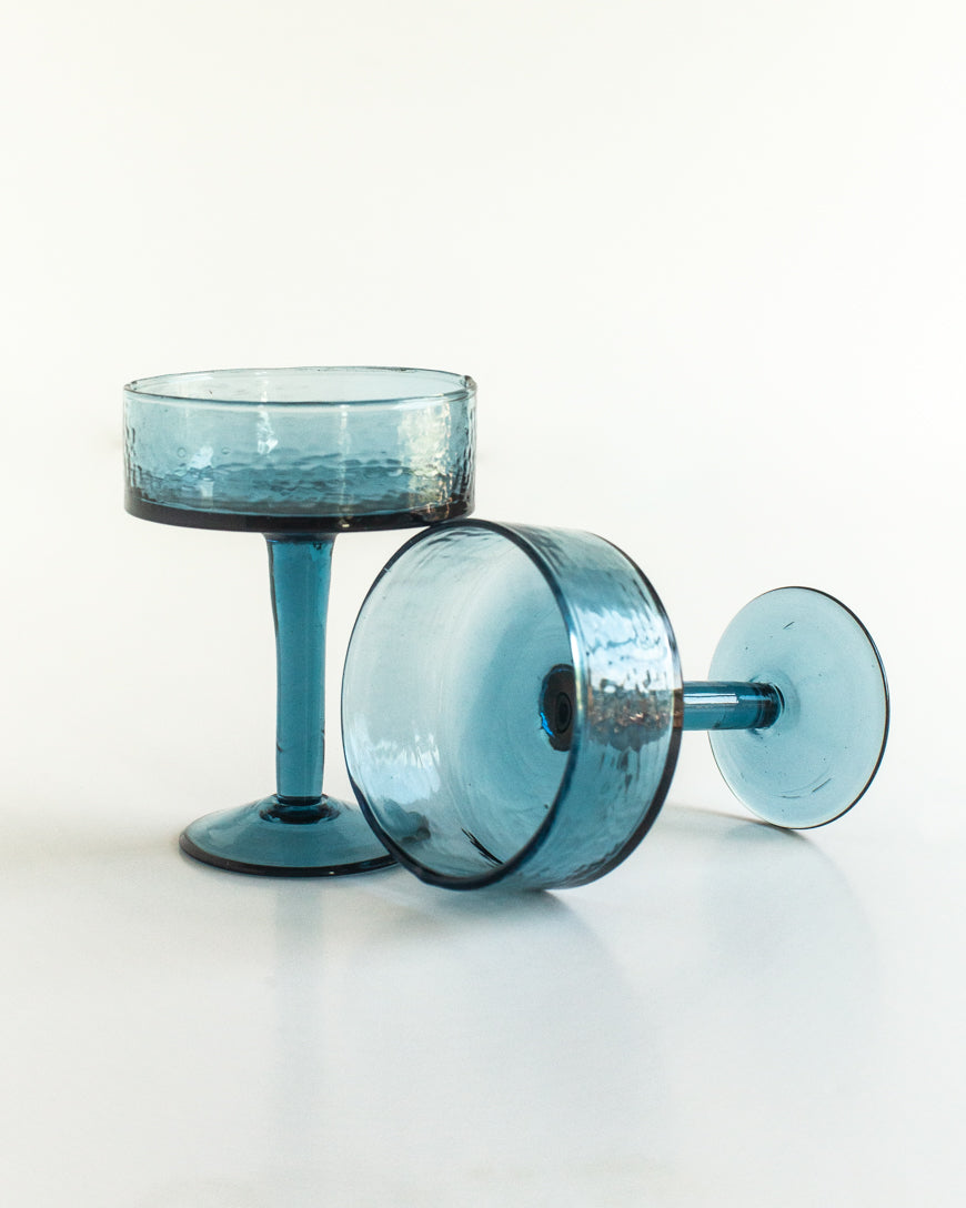Handblown hammered coupe cocktail glasses pair in colored recycled glass on a table