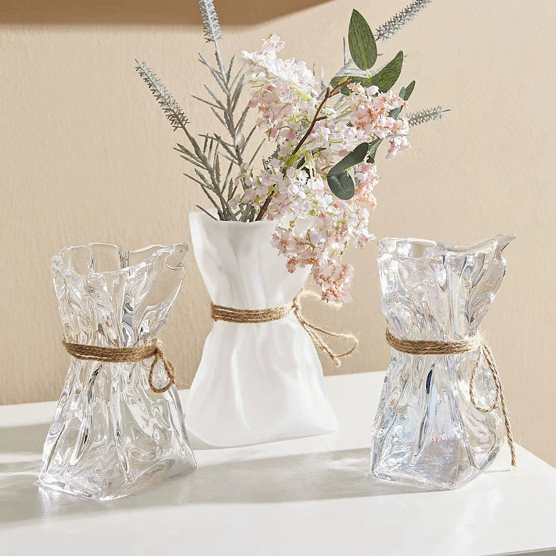 Wrinkled glass vase with natural twine accent and folded paper texture on a modern table