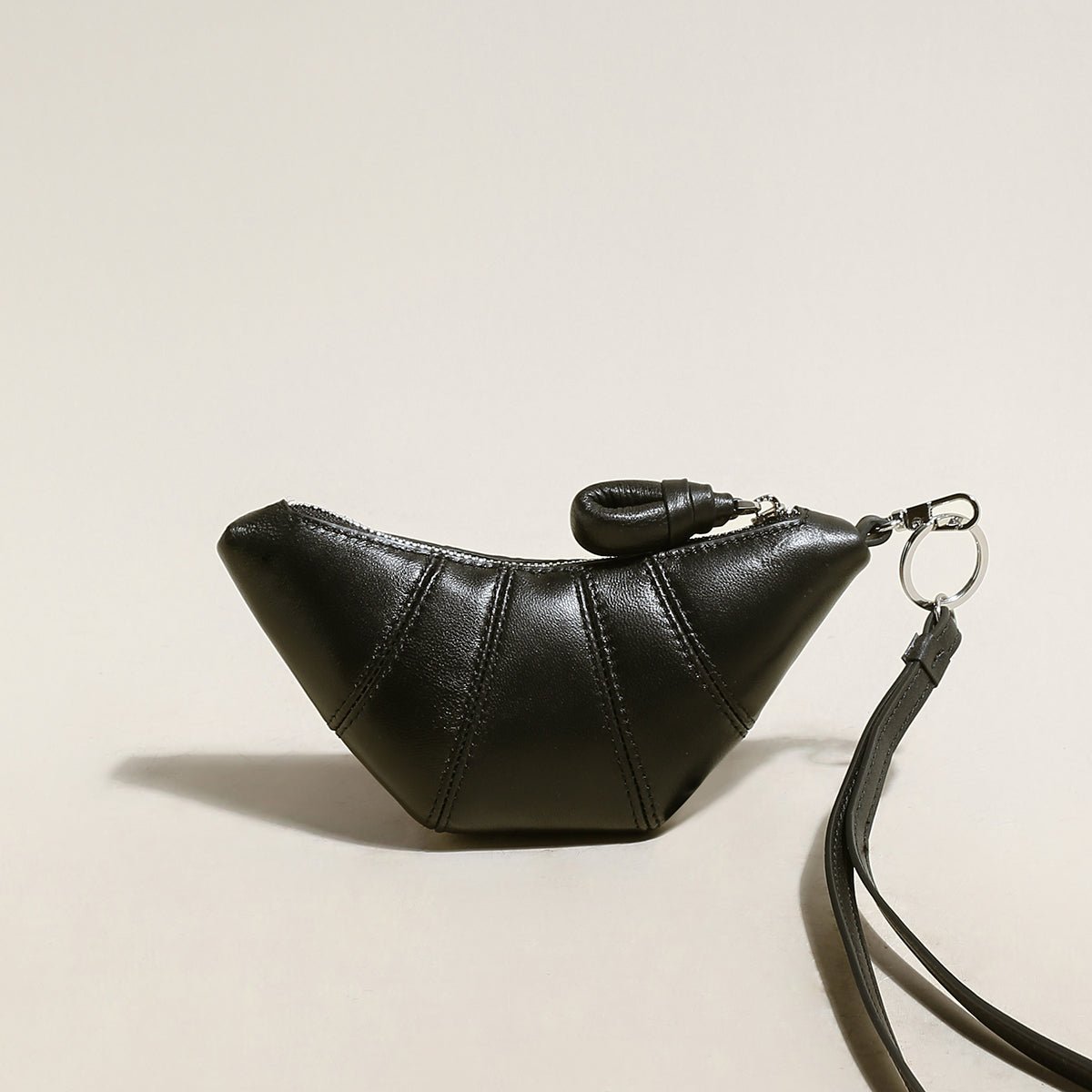 Soft vegan leather croissant mini pouch bag charm with wrist strap and zipper closure.