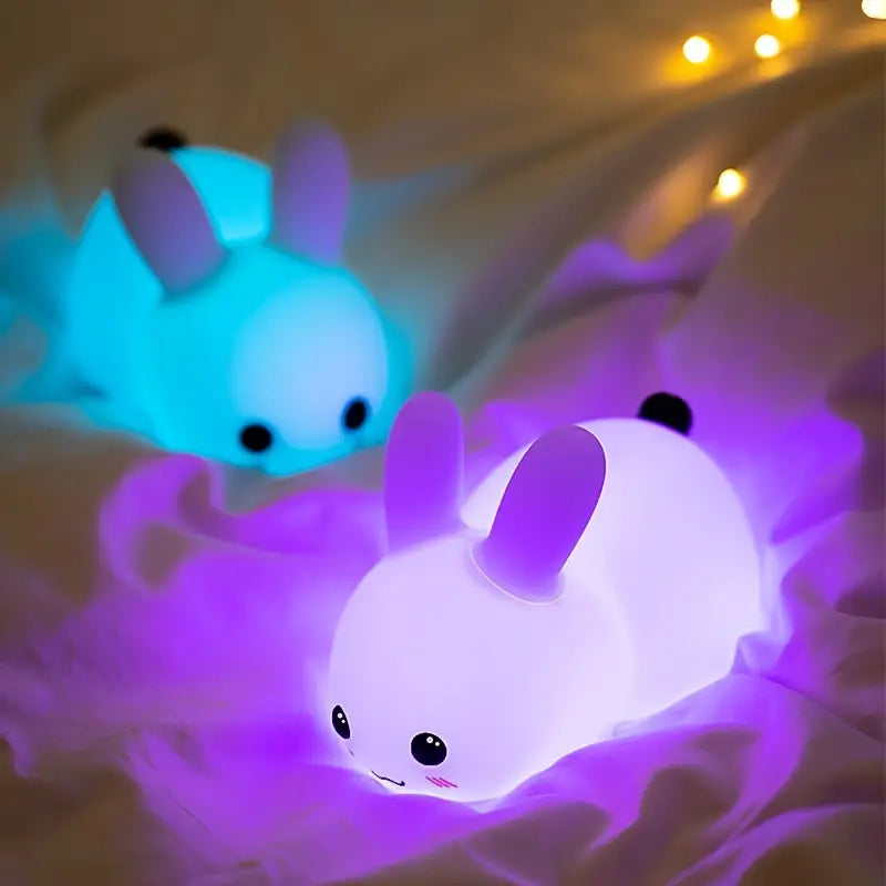 White squishy silicone bunny night light glowing with soft colors beside a remote control — view 4