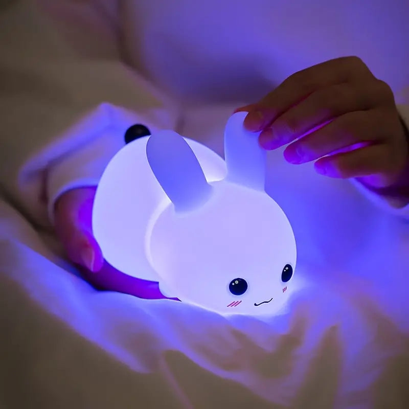 White squishy silicone bunny night light glowing with soft colors beside a remote control — view 5