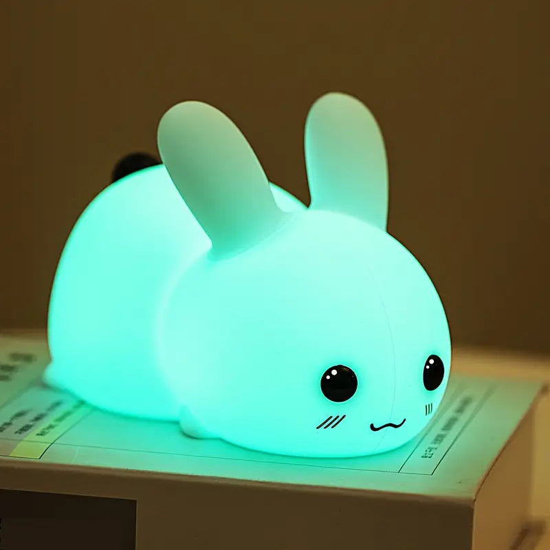 White squishy silicone bunny night light glowing with soft colors beside a remote control — view 2