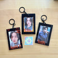 Clear acrylic photocard holder keychain displaying a card, with black chain and claw clasp.