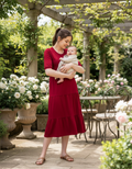 Burgundy cotton nursing midi dress featuring discreet zips, smock fit, and large pockets worn by model