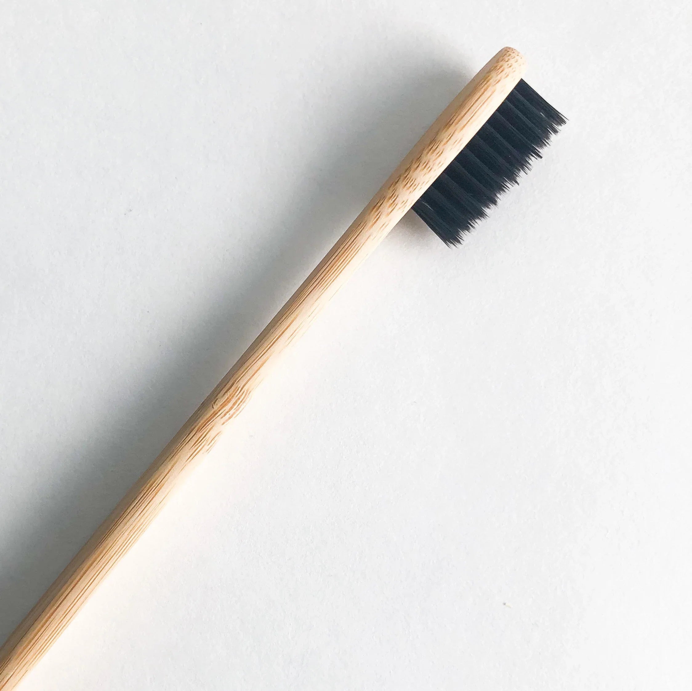 Bamboo charcoal toothbrush with black soft bristles and natural wooden handle on a clean background — view 4