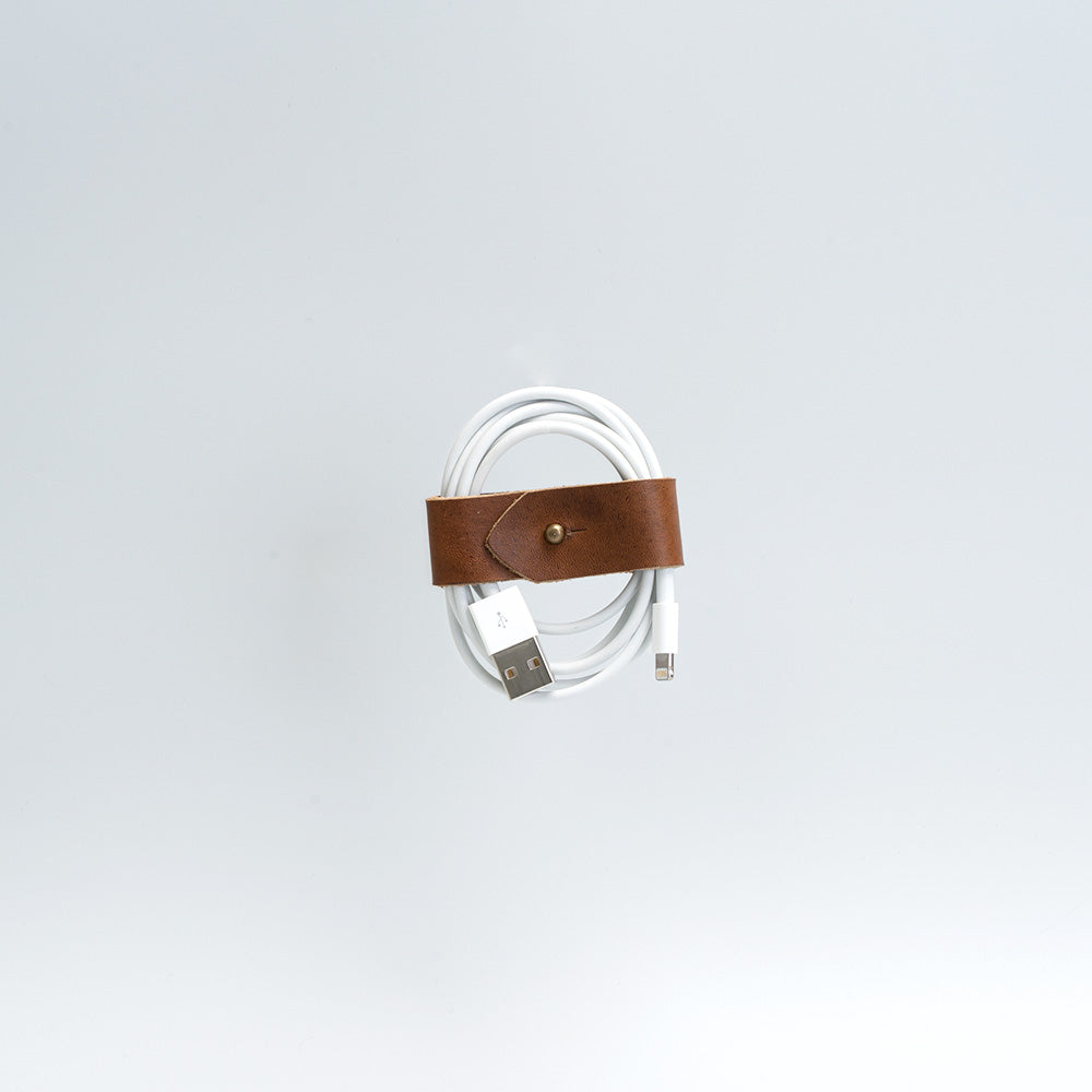 Handcrafted vegetable-tanned leather cord organizer securely wrapping a coiled white charging cable — view 4