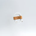 Handcrafted vegetable-tanned leather cord organizer securely wrapping a coiled white charging cable