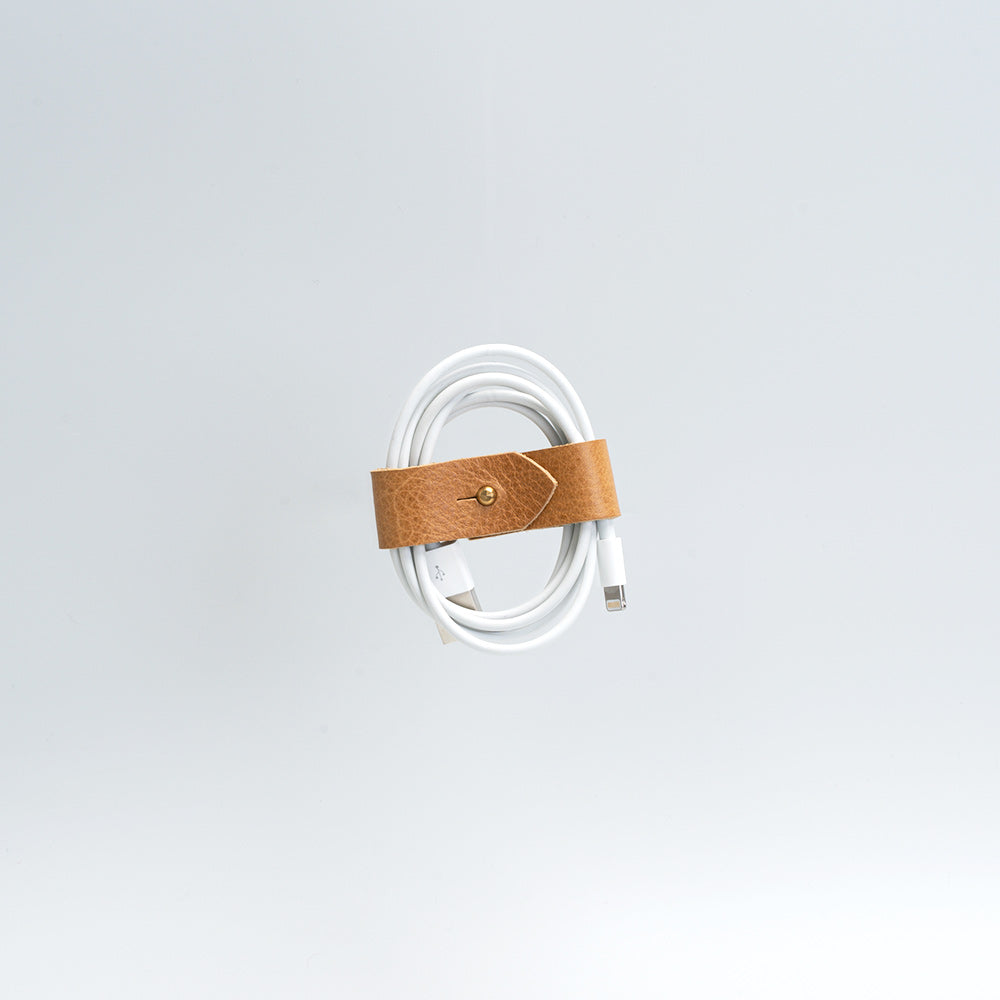 Handcrafted vegetable-tanned leather cord organizer securely wrapping a coiled white charging cable
