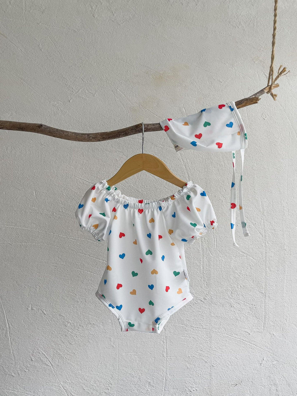 White baby girls one piece swimsuit with red hearts pattern and matching sun protection hat — view 2