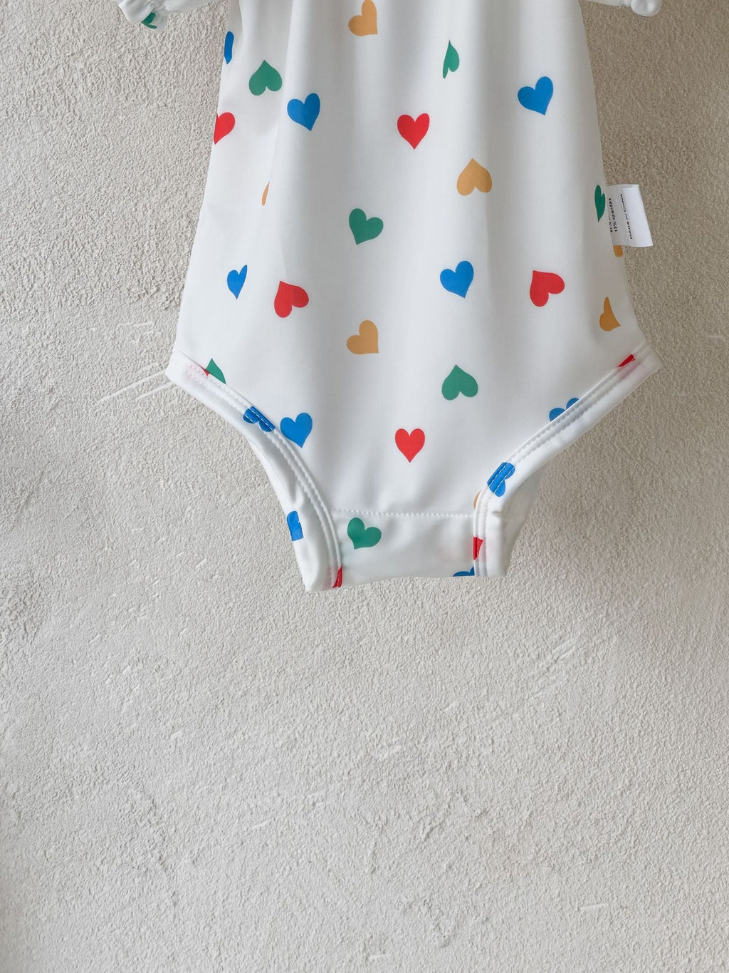 White baby girls one piece swimsuit with red hearts pattern and matching sun protection hat — view 3