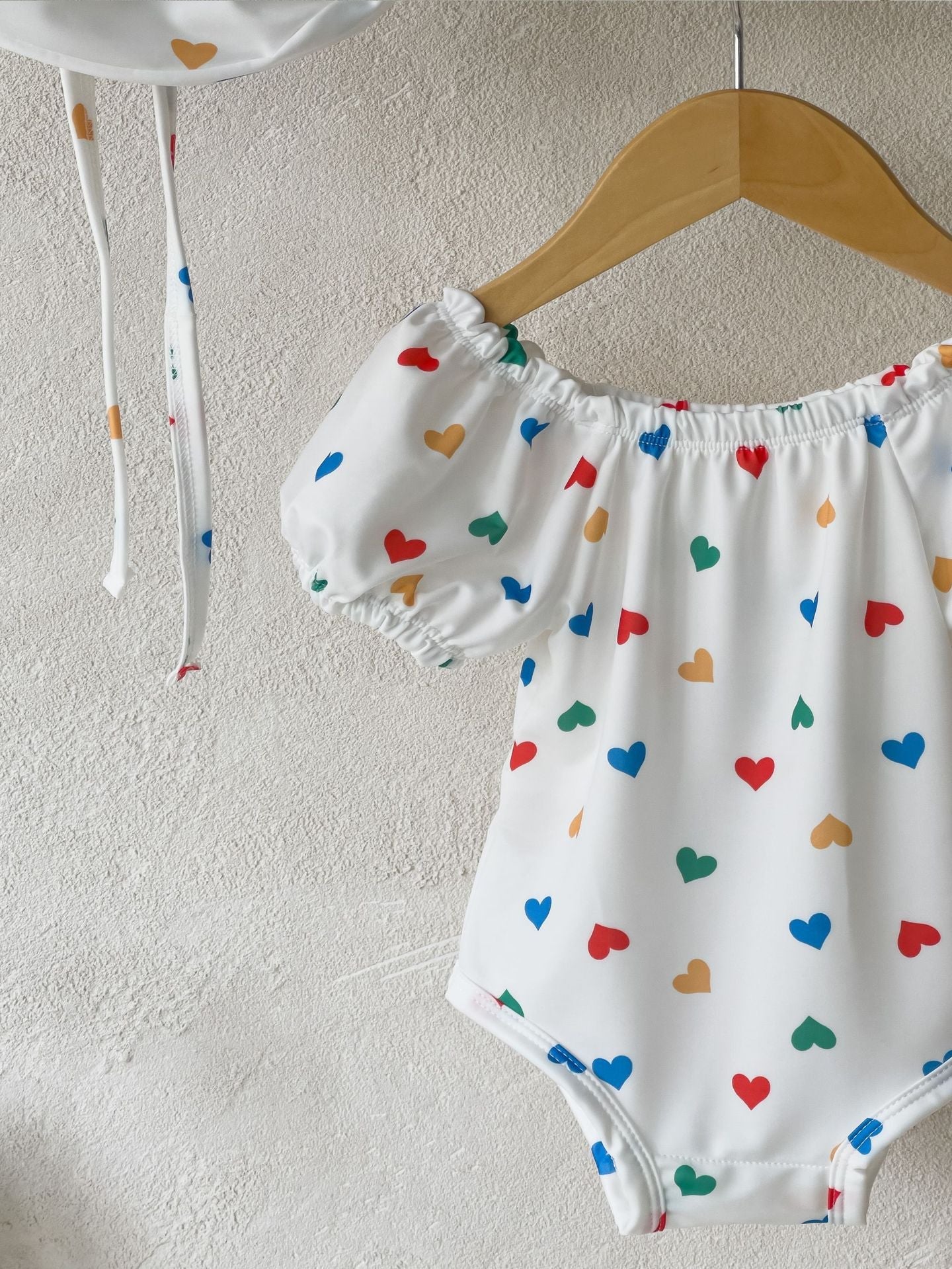 White baby girls one piece swimsuit with red hearts pattern and matching sun protection hat — view 4