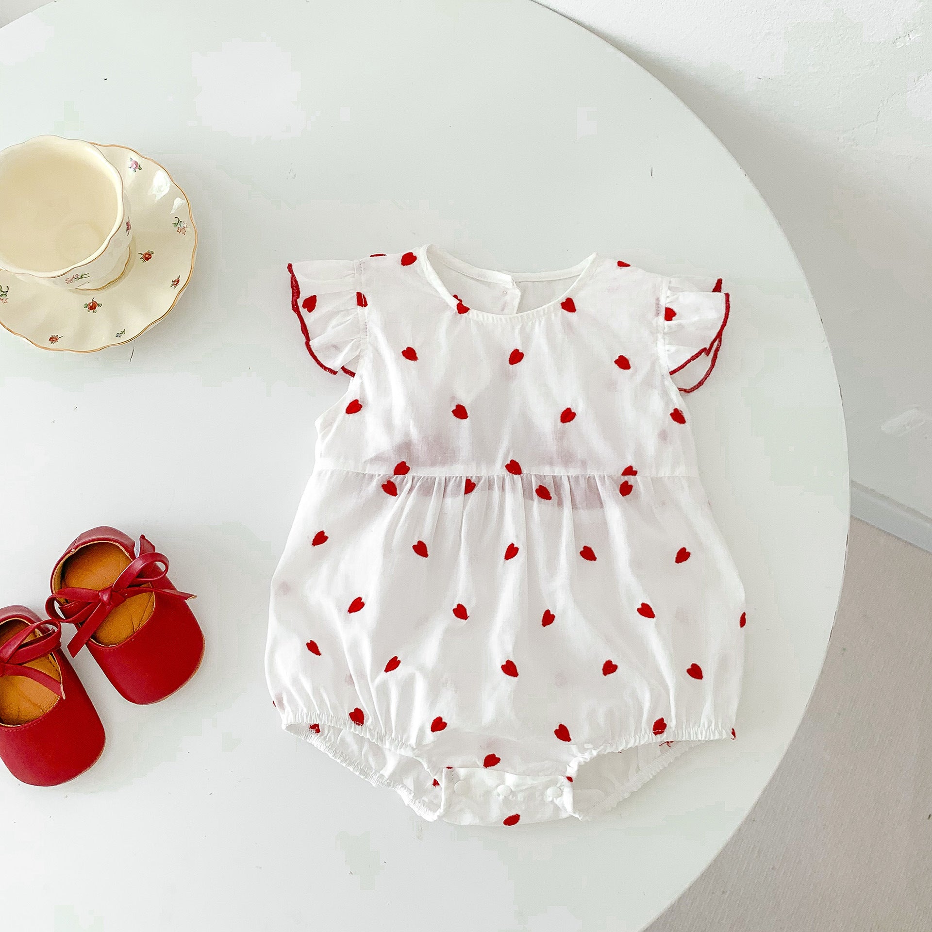 Baby girls beige summer bodysuit featuring a red heart print and delicate flutter fly sleeves.