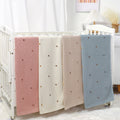Knitted cotton baby blanket with hand-embroidered pom poms, in soft solid colors for contemporary nurseries.