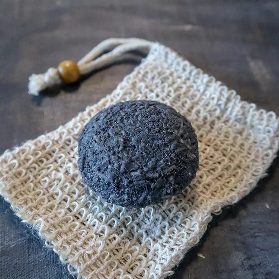 Solid charcoal rebalancing shampoo bar for oily hair placed on a natural wooden soap dish. — view 3