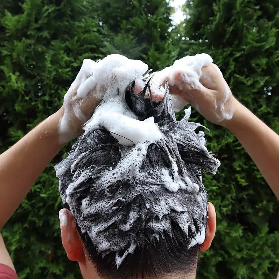 Solid charcoal rebalancing shampoo bar for oily hair placed on a natural wooden soap dish. — view 4