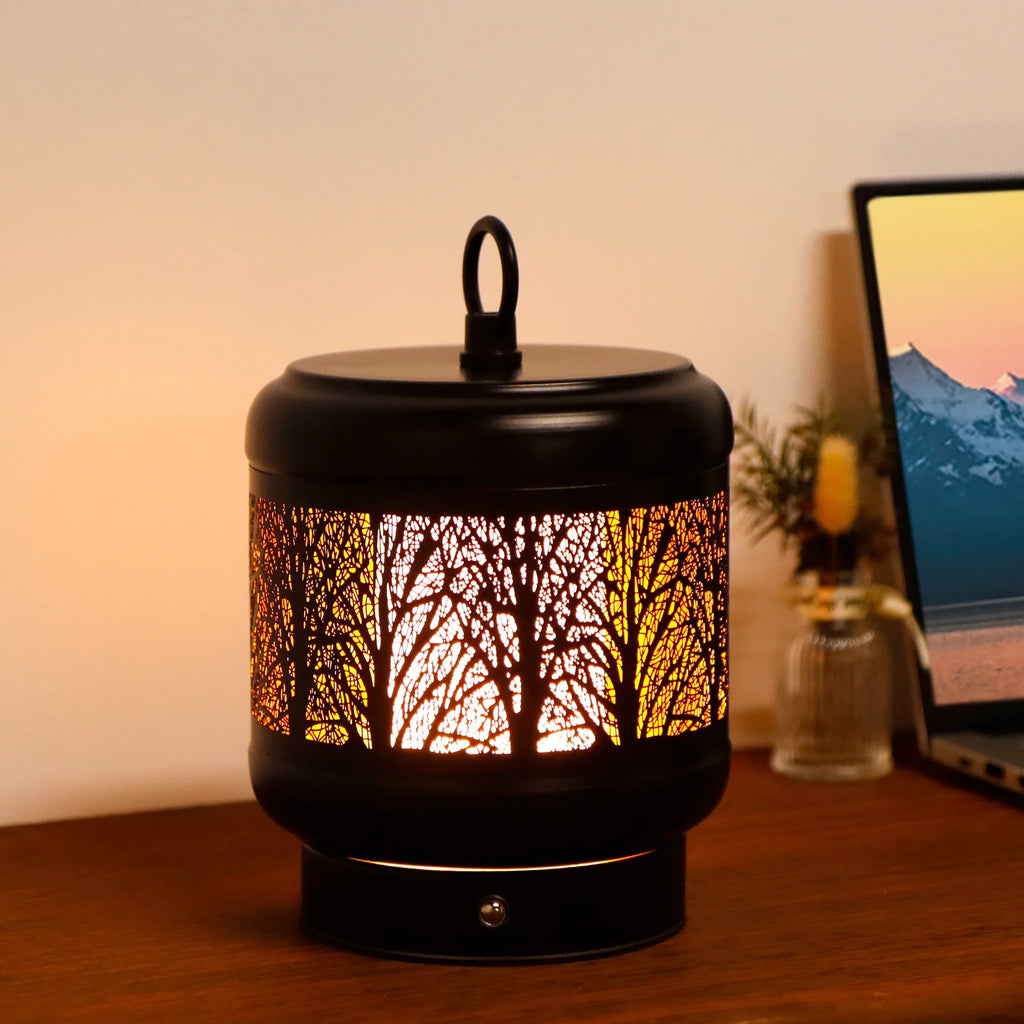 Rechargeable metal desk lamp with tree silhouette cutouts glowing in warm light on a table — view 3